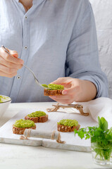 Female hand holds fork and put avocado cream on bread brown. 