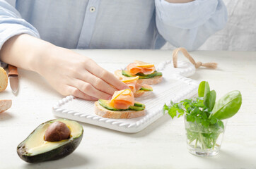 Female hand holds sandwich of salmon with avocado cream on light background.