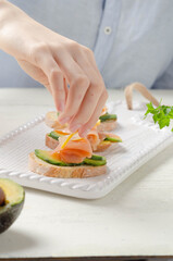 Female hand put salmon on sandwich with avocado cream.