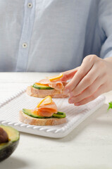 Female hand holds sandwich of salmon, avocado on light background. 