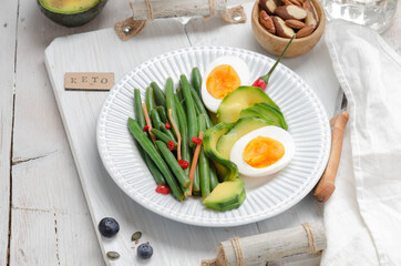 Green beans with avocado, egg and spices in a white dish on light background. Keto diet.