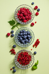 flat lay composition with different berries in glass bowls on green background with shadows. healthy eating, detox and vitamin concept. vertical image