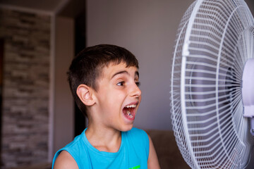 The little boy is cooling off in front of the fan