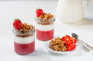 Yogurt with strawberry puree and granola in glass jars. Dessert.