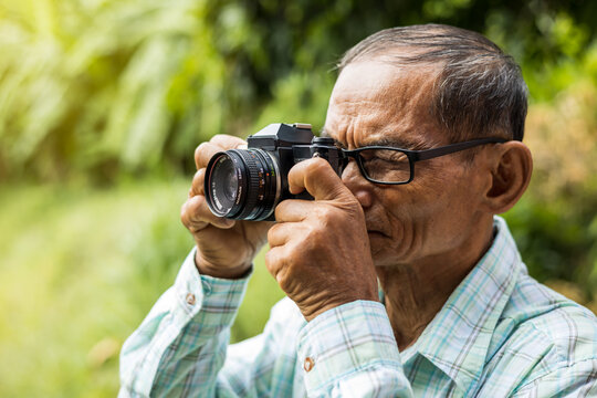 Close-up portrait of an elderly Thai man taking pictures with an old film camera.