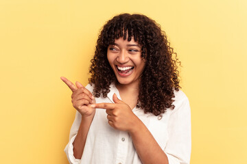 Young mixed race woman isolated on yellow background points with thumb finger away, laughing and carefree.