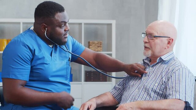 African-American caregiver and old disabled man in a wheelchair. Professional nurse and handicapped patient in a nursing home. Assistance, rehabilitation and health care.
