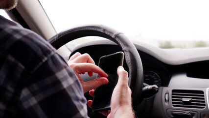 a man sits in a car with a mobile phone in his hand and writes text messages while driving