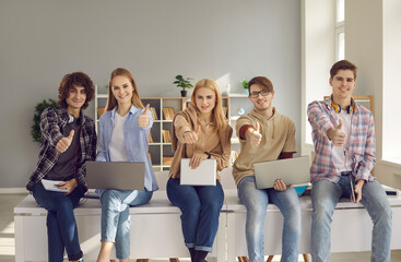 Group of happy high school, college or university students with laptops and tablets looking at...