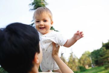 young mom kisses her little son while sitting in the park on the lawn