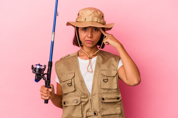 Young mixed race fisherwoman holding a rod isolated on pink background pointing temple with finger, thinking, focused on a task.