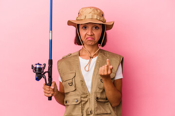 Young mixed race fisherwoman holding a rod isolated on pink background pointing with finger at you as if inviting come closer.