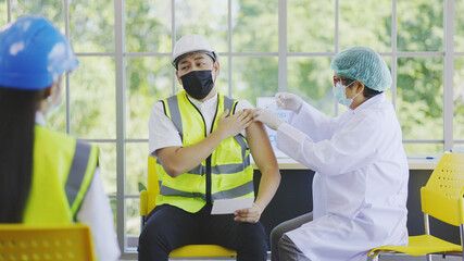 COVID-19 Vaccination station in construction industry. Doctor are vaccinating to group engineer...