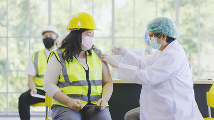 COVID-19 Vaccination station in construction industry. Doctor are vaccinating to group engineer...