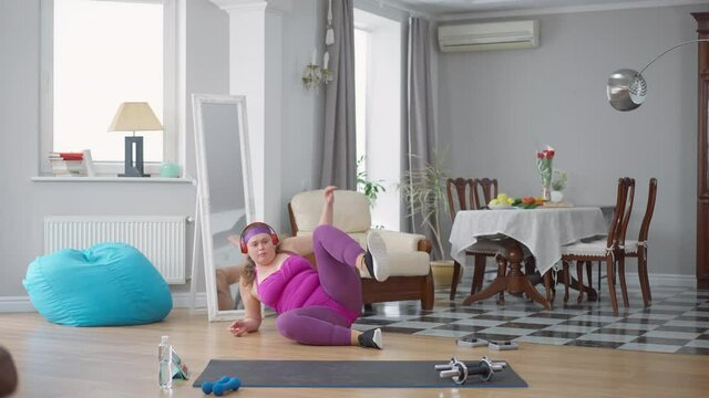 Obese Caucasian young woman falling jumping with skipping rope and walking away. Wide shot of upset overweight plus-size lady dissatisfied with morning workout at home indoors. Failures concept