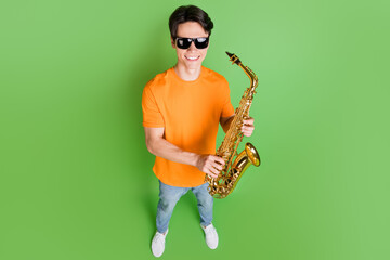 Full size top high above angle view photo of young happy man hold hand saxophone isolated on green...