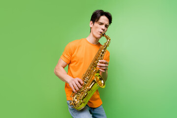 Photo of joyful happy young man hold hands play saxophone jazz lover isolated on green color background