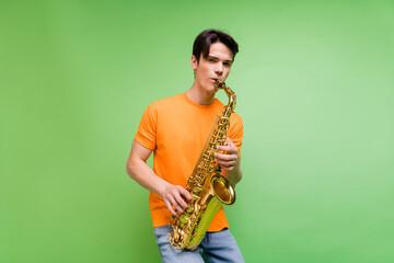 Photo of charming positive happy man hold hands saxophone musician isolated on green color...