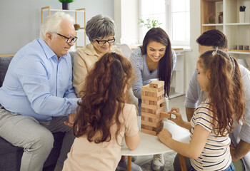 Family weekend entertainment. Happy big family plays Jenga at home and takes turns taking bricks...