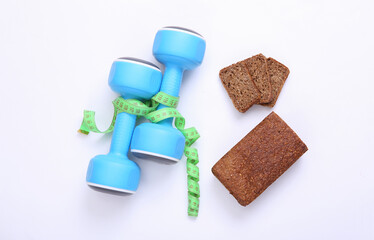 Measuring tape and dumbbells, diet whole grain rye bread on a white background. Weight loss, diet, fitness concept