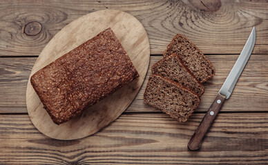 Sliced whole grain rye bread with knife on wooden background