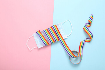 Medical mask with LGBT rainbow ribbon tape on blue pink background.