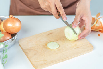 Woman cutting fresh onion on wooden board in kitchen. prepare to cook.