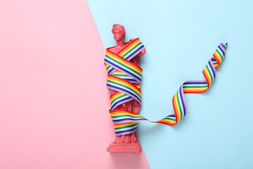 Ancient Greek goddess statue with LGBT rainbow ribbon pride tape symbol on pink blue background. Top view