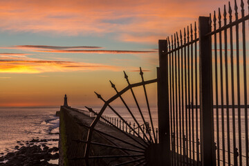 Tynemouth Pier and the Lighthouse through the metal railings with a beautiful vibrant sunrise