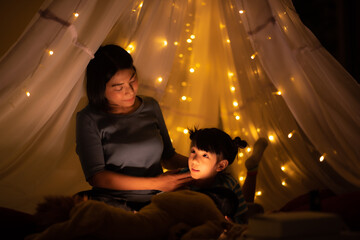 mom and kid bedtime story in illuminated children's tent, happy quality time, family concept dark...
