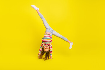 Full length photo of happy flexible little girl enjoy active weekend upside down isolated on yellow...