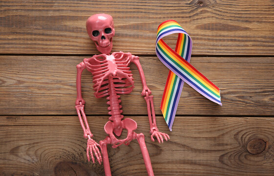 Pink skeleton with LGBT rainbow ribbon pride tape symbol on wooden background. Top view