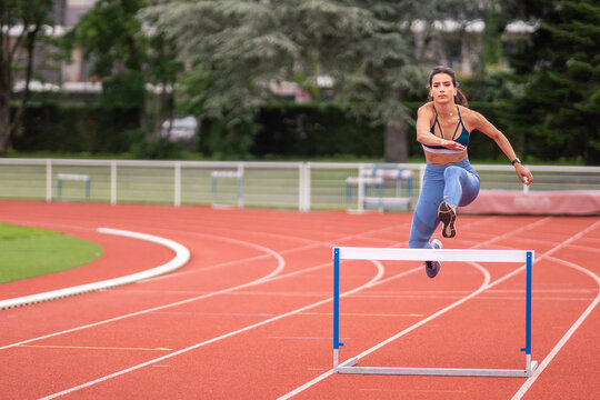 Female athlete jumping over hurdle at stadium