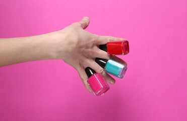 Female hand holding nail polishes between fingers on pink background