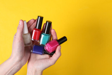 Female hands holding nail polish bottles on yellow background