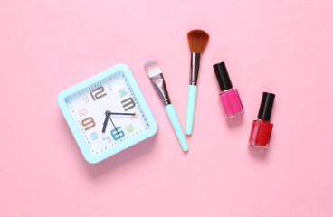 Makeup products and alarm clock on a pink background. Top view