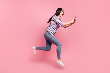 Full length photo of cute pretty young lady dressed checkered shirt typing modern gadget jumping high isolated pink color background