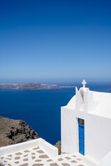 Fototapeta na wymiar Santorini island. View of caldera at sunny day. Small minimalistic Greek Orthodox Church. White cross.