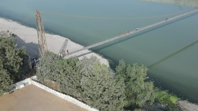 Drone flies high in the sky above floating clouds. Below, overlooks an impressive view of the Hanging bridge near machhu dam, Aerial. 4K