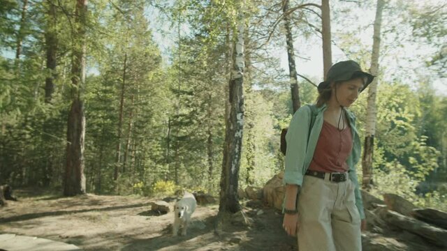 Young woman walking in woods on sunny summer day, then sitting in travel trailer and petting cute dog
