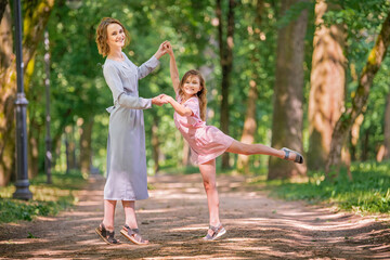 Naklejka na ściany i meble Mother and daughter are playing dancing in park. Happy family concept. Beauty nature scene with family outdoor lifestyle. Happy family resting together. Happiness and harmony in family life.