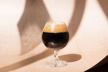Glass of dark beer, on the beige background with interesting shadows. Minimal still life with copy...