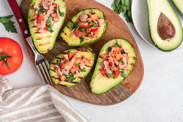 Grilled avocado stuffed with tuna, tomatoes, parsley, and olive oil on a cutting board. Top view, grey background