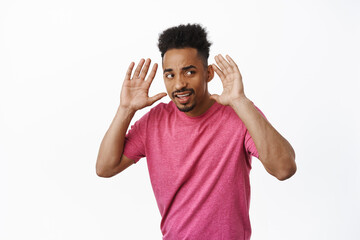 Intrigued african american man trying to overhear gossip, holding hands near ears and looking...