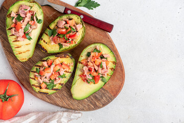 Grilled avocado stuffed with tuna, tomatoes, parsley, and olive oil on a cutting board. Top view, grey background