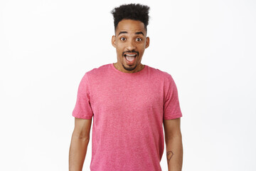 Obraz premium Image of excited and surprised young african american guy, looking thrilled and amused, checking out big news, smiling amazed, standing in pink t-shirt against white background