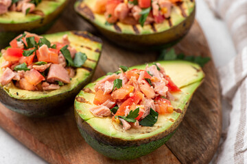 Grilled avocado stuffed with tuna, tomatoes, parsley, and olive oil on a cutting board. 