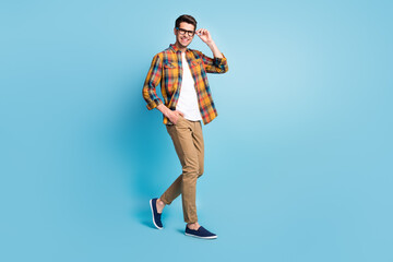 Fototapeta na wymiar Photo of pretty attractive young gentleman wear checkered shirt arm glasses walking smiling isolated blue color background