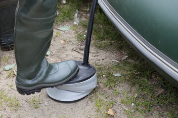A man's foot in a rubber boot pumps an inflatable boat with a foot air pump