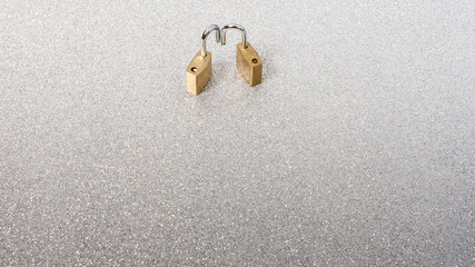 Fototapeta na wymiar Silver background and two golden padlocks that pretend to show an idea.The photo has a large copy space to put text or whatever you want.The photograph is taken in horizontal format.